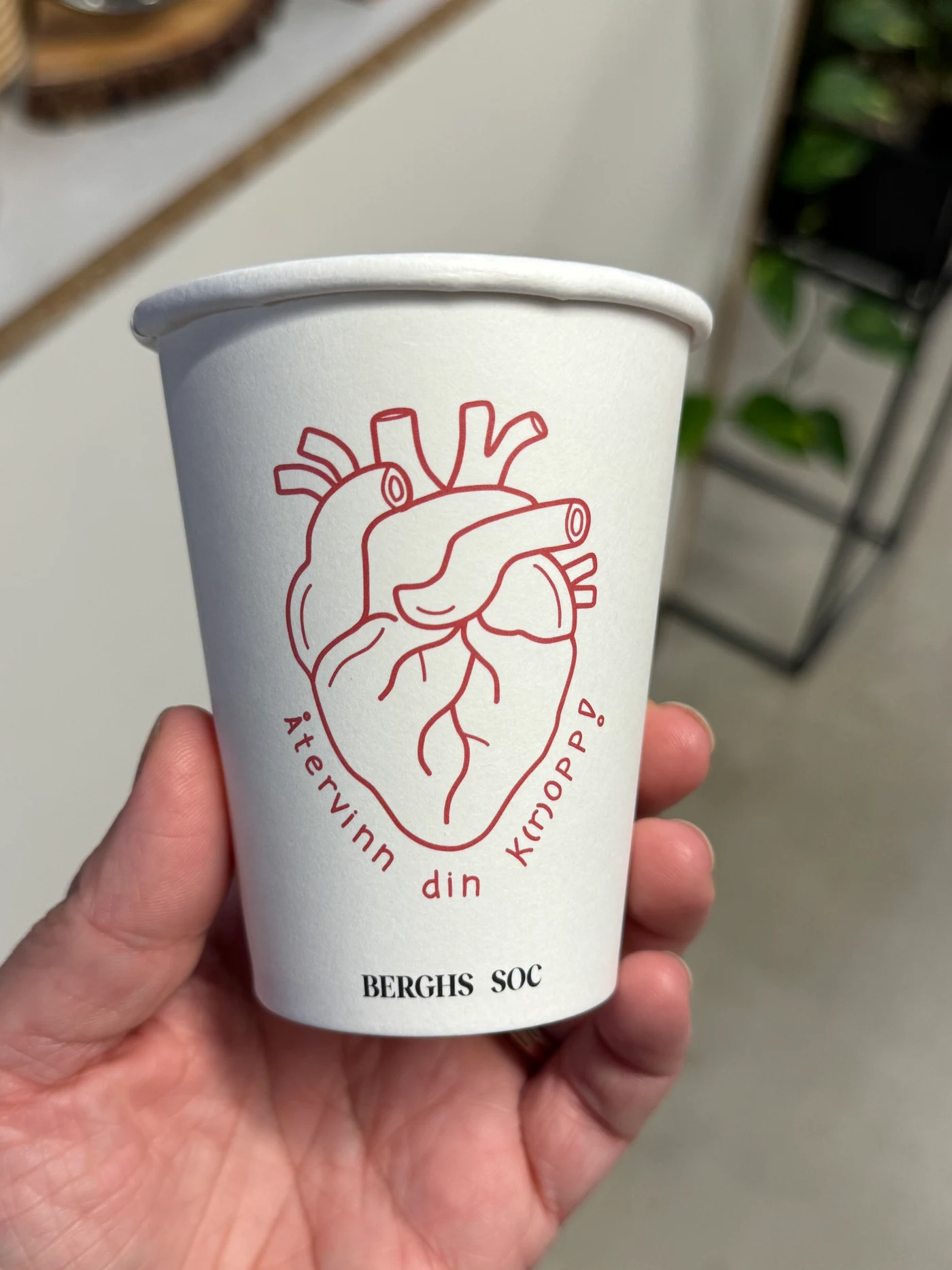 A finished Berghs coffee cup held in a hand, showing the printed red heart illustration.